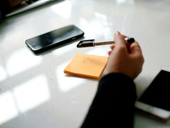 Cropped hand of businesswoman holding pen over sticky notes by mobile phones on table