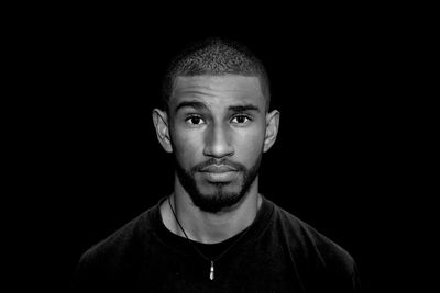 Close-up portrait of man standing against black background