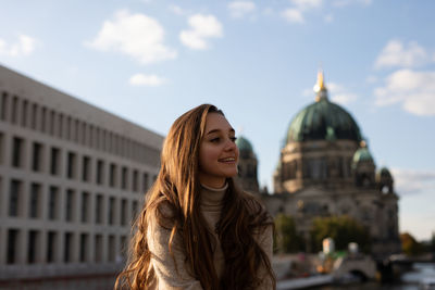 Smiling young woman standing against buildings in city