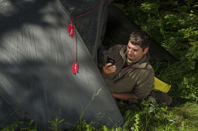 High angle view of man using phone while lying in tent