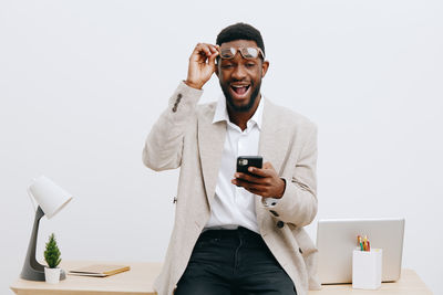 Portrait of young man using mobile phone while standing against white background