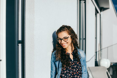 Portrait of smiling young woman standing by wall