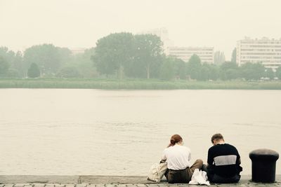 Rear view of men sitting by lake against sky