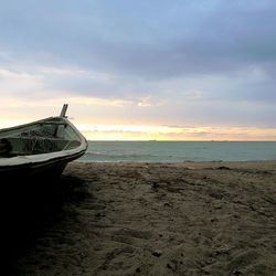 Boat moored on beach against sky during sunset