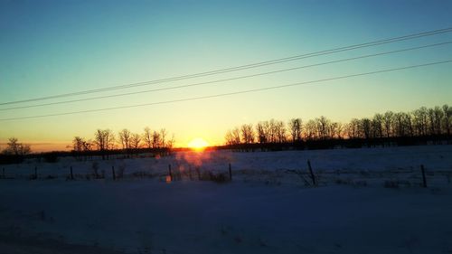 Silhouette trees on snow against sky during sunset