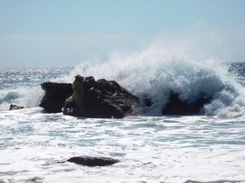 Waves splashing on rocks against sky