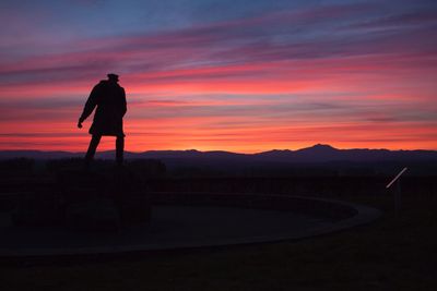 Silhouette of man standing on landscape against sky during sunset