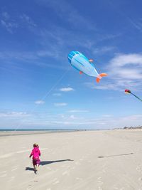 Rear view of girl running at beach against sky during sunny day