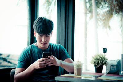Young man using mobile phone while sitting on table