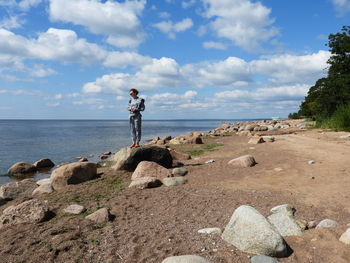 Man standing on rock by sea against sky