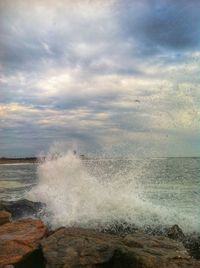 Waves splashing on rocks against cloudy sky