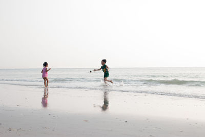 Siblings playing on shore at beach against sky