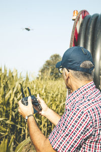 Man flying drone while standing amidst plants against clear sky