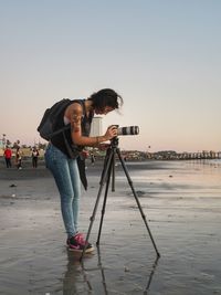 Woman photographing on beach against clear sky