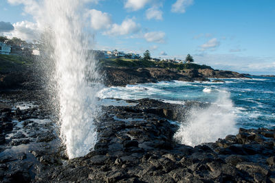 Waves splashing on rocks against sky