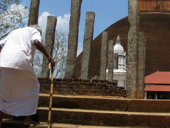 Rear view of senior man walking cane on steps of temple