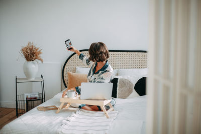 Young woman using laptop while sitting on bed at home