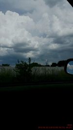 Road passing through field against cloudy sky