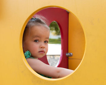 Portrait of cute baby girl sitting in outdoor play equipment at playground