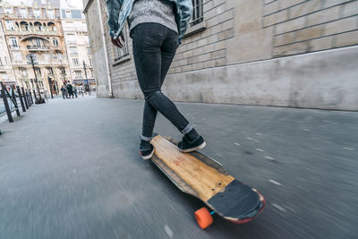 Low section of woman skateboarding on footpath in city