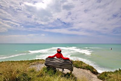 Rear view of woman looking at sea while sitting on bench