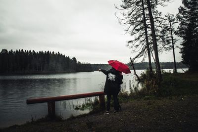 Couple with umbrella standing at riverbank against sky