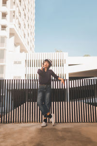 Portrait of teenage girl standing on railing against sky