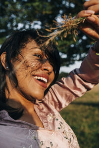 Cheerful woman holding grass on sunny day