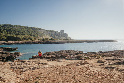 Rear view of person standing by sea against clear sky