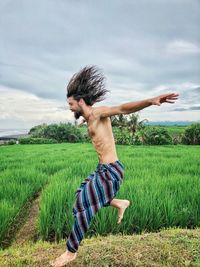 Midsection of shirtless man standing on field against sky