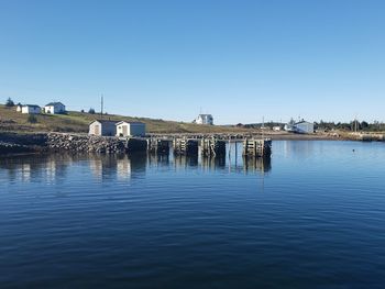 Bridge over river by buildings against clear blue sky