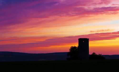 Silhouette built structure against orange sky
