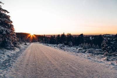 Snow covered road against sky during sunset