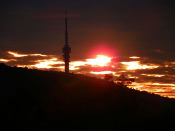 Silhouette of communications tower against cloudy sky