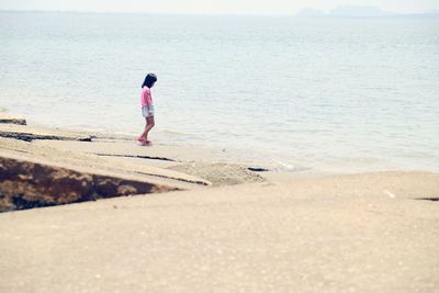 Rear view of boy standing on beach against sky