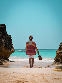 Rear view of woman standing at beach against clear blue sky