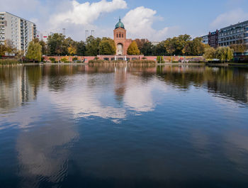 Reflection of church in front of river against sky