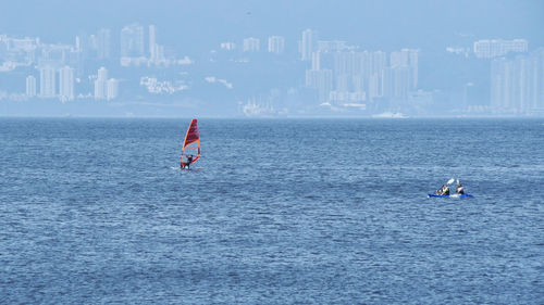 People on sea by city against sky