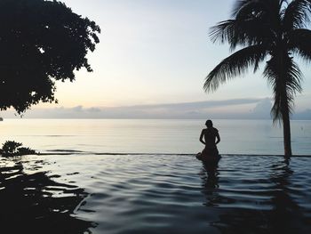 Rear view of woman relaxing at infinity pool against sea