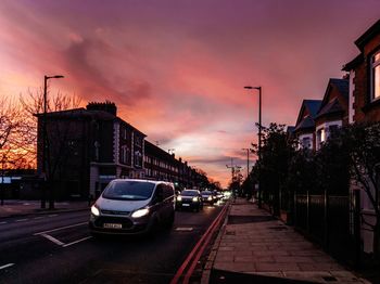 Cars on street in city against sky at sunset