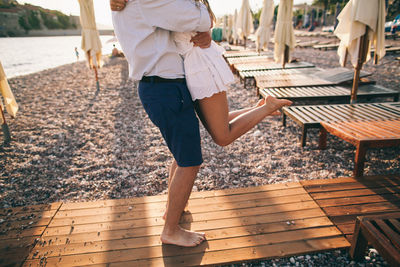 Low section of man lifting woman while standing on wood at beach
