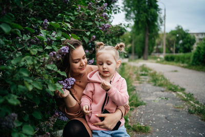 Mom hugs baby daughter lilac flowers outdoor nature