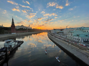 River amidst buildings in city against sky during sunset