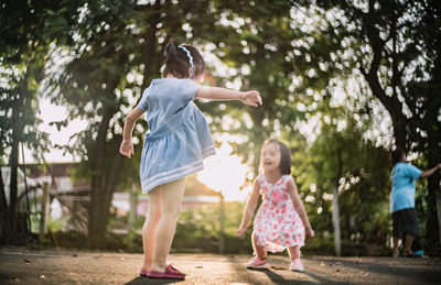 Siblings playing on road by trees