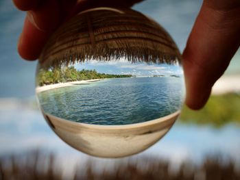 Cropped hands holding crystal ball with sea reflection