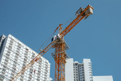 Low angle view of tower crane by building against clear sky