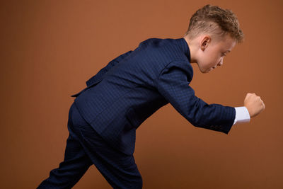 Side view of boy gesturing against brown background