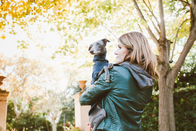 Rear view of woman holding dog standing outdoors