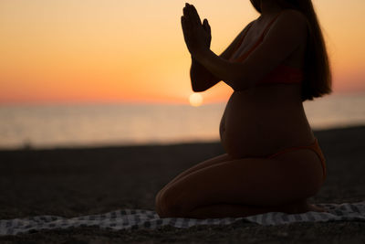 Silhouette of pregnant woman wearing swim suit doing yoga at beach near sea at sunset 