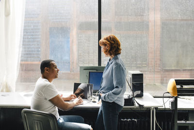 Male technician discussing with senior female customer standing near desk at repair shop